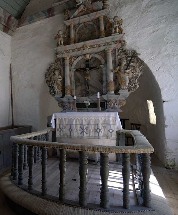 Färgfoto på altare med pampig och dekorerad altaruppsättning. Den når nästan till taket och täcker absiden. I förgrunden en altarring.