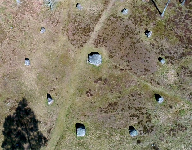 Flygfoto. 11 stenbumlingar i en cirkel som är cirka 15 meter i diameter. I centrum en större sten.