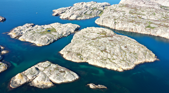 Färgfoto från luften på närmast kala öar med omgivna av blått vatten.