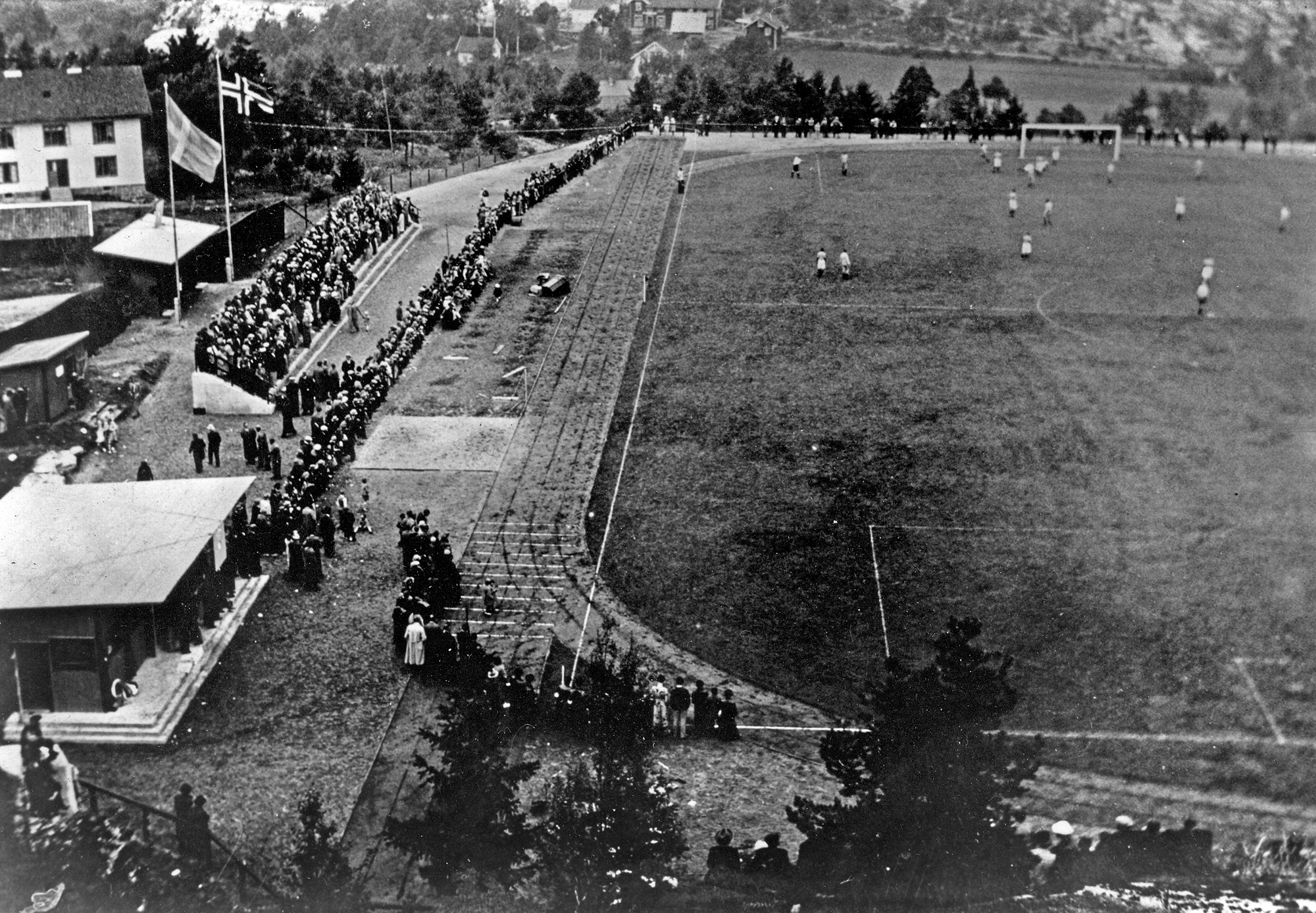 Äldre svartvitt foto med fotbollsplan, spelare och publik.