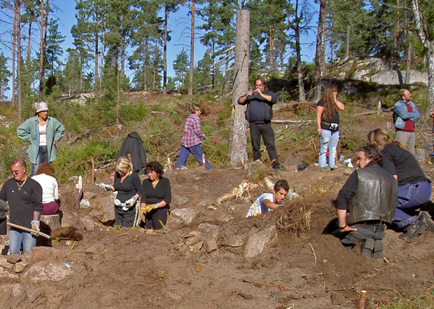 Färgfoto med ett antal personer som är sysselsatta i och runt en stor grop som är röjd från växtlighet.