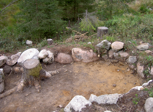 Färgfoto av en sandig yta som bildar ett litet rum avgränsat av en låg stenmur.