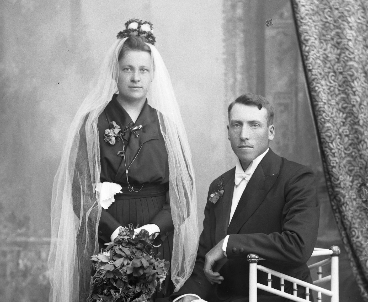 Svartvitt foto av brudpar. Bruden har svart klänning, vit slöja och myrtenkrona. 