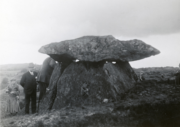Svartvitt foto visar stora resta stenblock med en takhäll över i ett kalt landskap. En kivnna och en man står bredvid.
